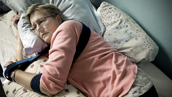 Kvinde ligger i en seng med sin arm i en slynge.